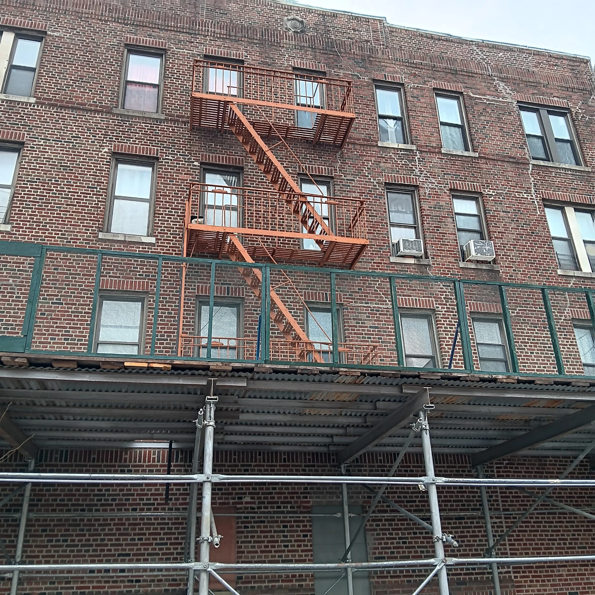 Fire escape painting NYC on brick building with sidewalk shed for safety and rust protection